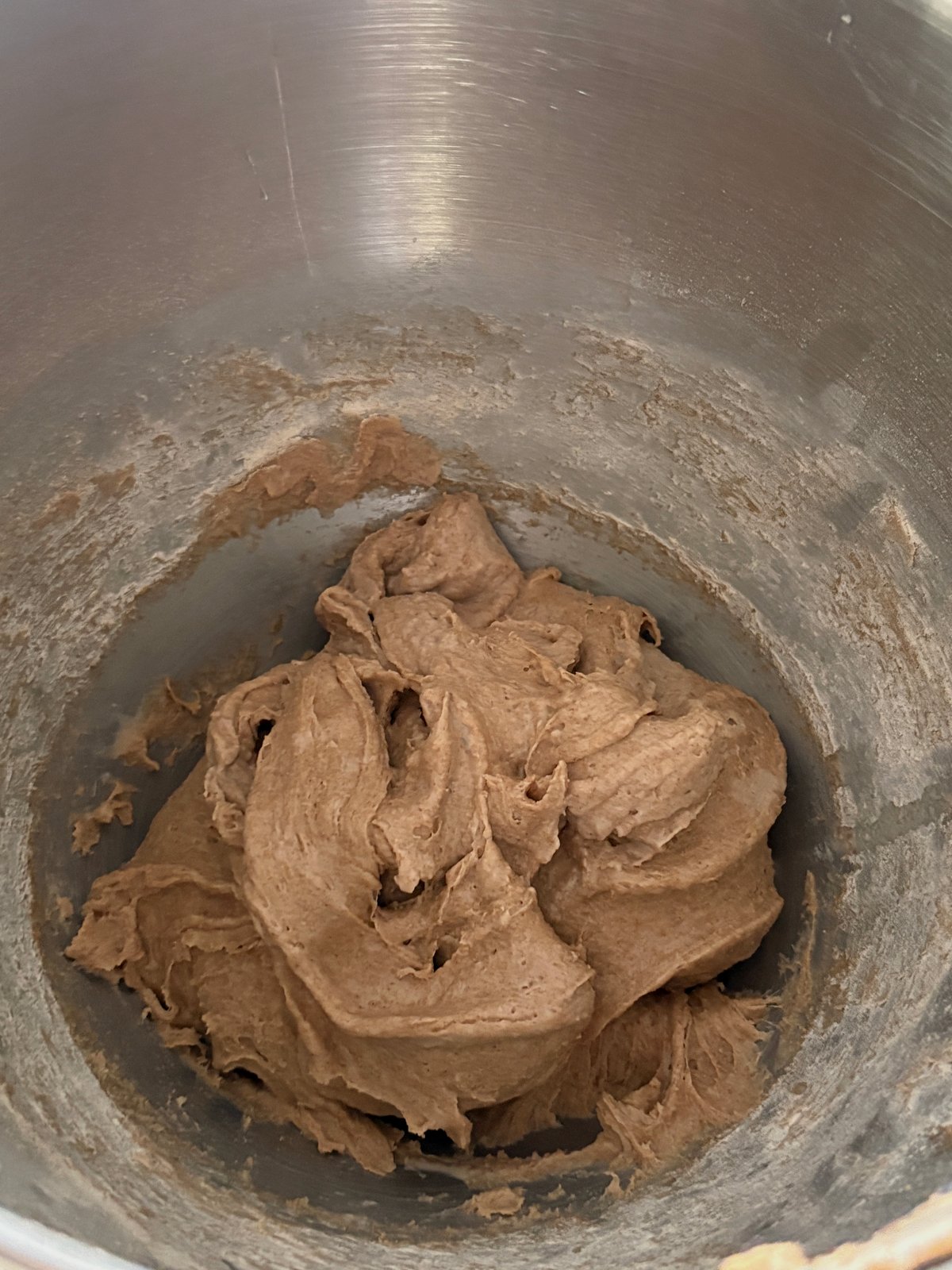 Tan whole wheat dough in a mixer bowl, one mass with torn hook ridges and wet creases